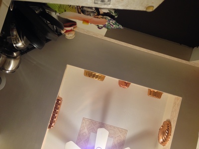 [A shot of a kitchen ceiling, which includes a pan rack, and some decorative copper molds flanking a ceiling fan.] Everything is looking up.  Of course, that's easy to say when one is flat on their back on the kitchen floor.