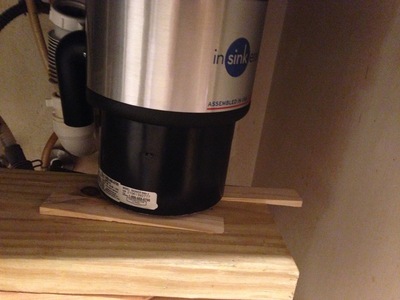 [Picture of a garbage disposal, sitting on some wedges, several pieces of wood, and a small foot stool I couldn't fit into the shot.  Also, there's a drain pipe hanging off the left side of the unit.] See that black thing hanging off the left side?  Yes, that's the drain pipe.  That's going to prove to be problematic in a few moments.