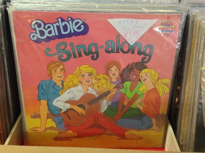 [A picture of the “Barbie Sing-along” vinyl record, with Barbie, Ken, and three kids, one of which is darker than the other two] ♫One of these things is not like the others, / One of these things just doesn't belong, / Can you tell which thing is not like the others / By the time I finish my song?♫