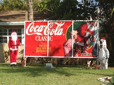 [Huge, three-panel display of a vintage Coca-Cola Santa Ad flanked by a life-sized Santa on the left, and maybe a yeti on the right, in the front yard of a house in the neighborhood] Either Sasquatch is planning an Artic expedition, and thus shilling for Coke for funding, or else he's really old and trying to raise retirement funds by shilling for Coke.  In either case, we know Santa has been a sell out for mostly a century now.