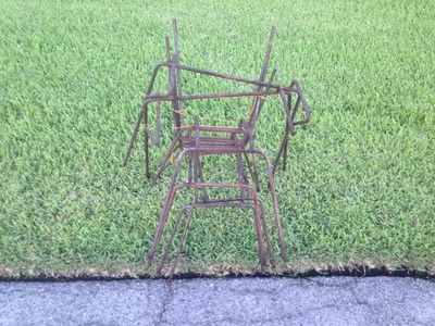 [A well manicured lawn next to the street, with a collection of metal rods all askew forming some form of structure] It kind of, sort of, looks like a headless version of the Burning Man sculpture.  Or perhaps a loose interpretation of a Feynman Diagram.  Hard to say …